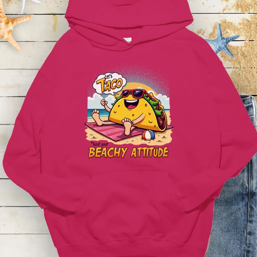 Heliconia hoodie with a taco wearing sunglasses laying on a beach towel on the beach with the text Let's Taco 'bout your Beachy Attitude.