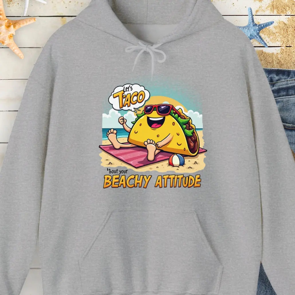 Gray hoodie with a taco wearing sunglasses laying on a beach towel on the beach with the text Let's Taco 'bout your Beachy Attitude.