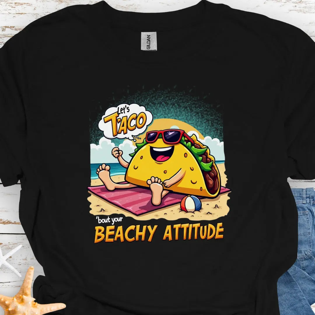 Black t-shirt with a taco wearing sunglasses laying on a beach towel on the beach with the text Let's Taco 'bout your Beachy Attitude.