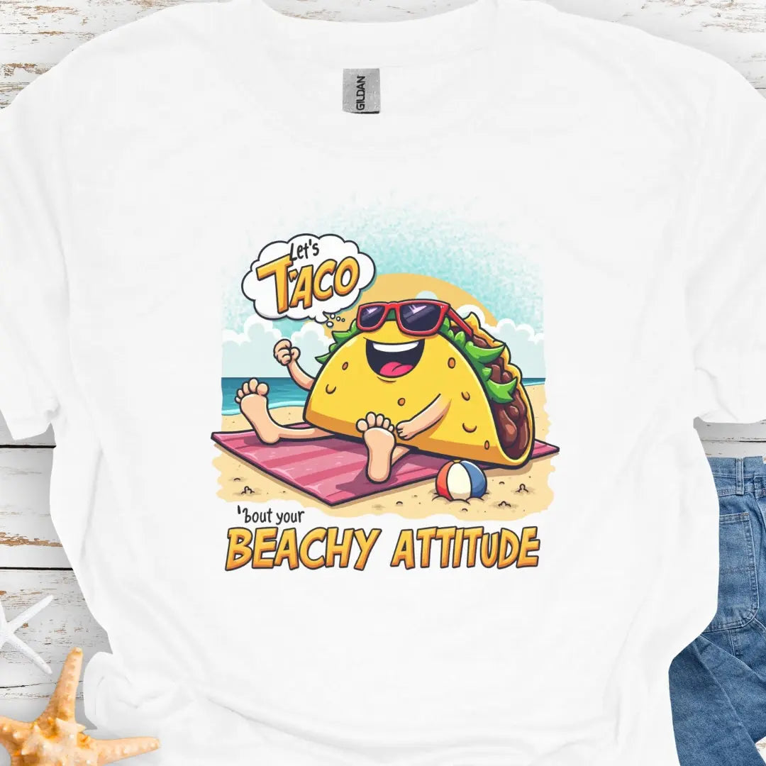 White t-shirt with a taco wearing sunglasses laying on a beach towel on the beach with the text Let's Taco 'bout your Beachy Attitude.
