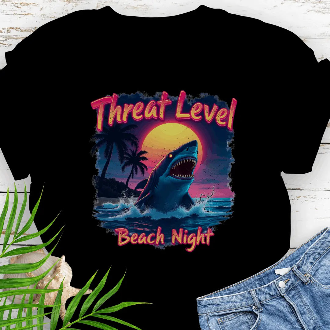 Black T-shirt with the words Threat Level Beach Night and a shark coming out of the ocean with a bright moon background in a retro 80's movie poster vibe.