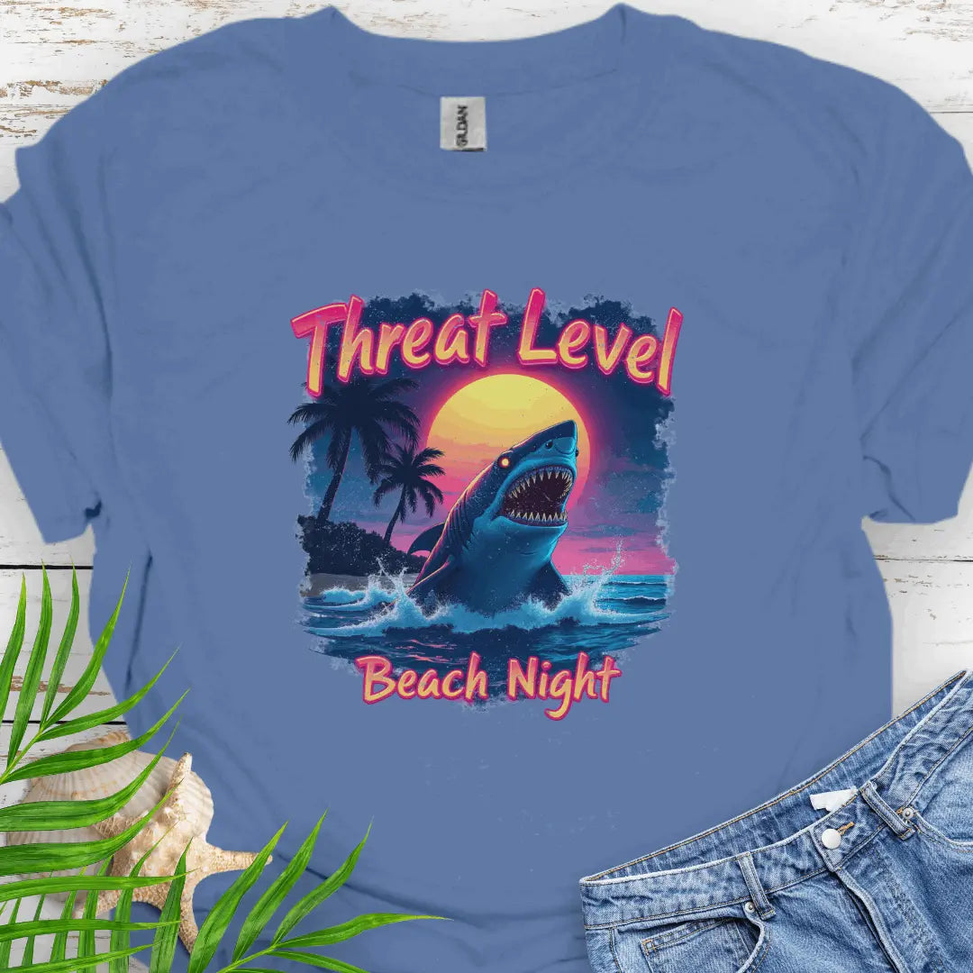 Indigo Blue T-shirt with the words Threat Level Beach Night and a shark coming out of the ocean with a bright moon background in a retro 80's movie poster vibe.