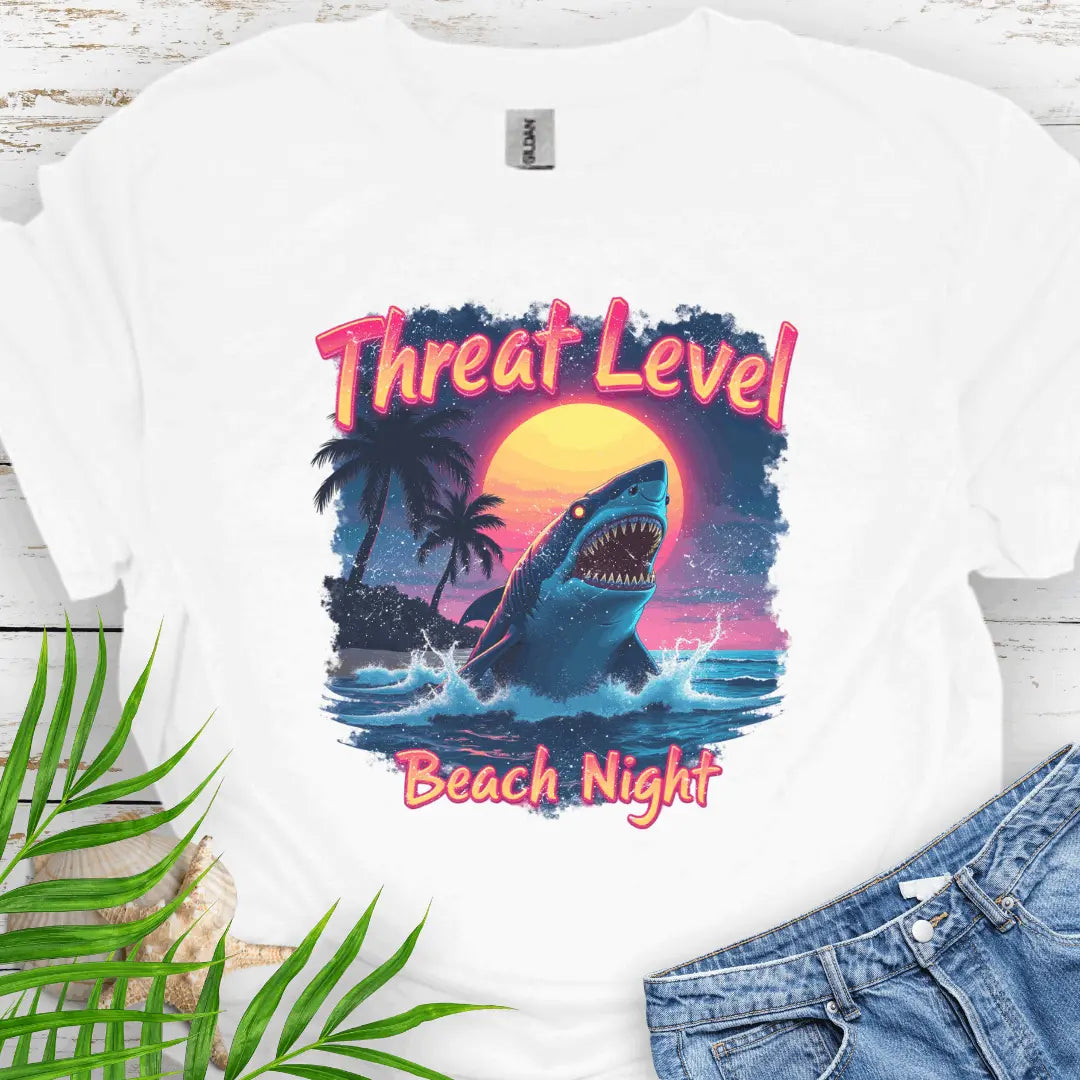 White T-shirt with the words Threat Level Beach Night and a shark coming out of the ocean with a bright moon background in a retro 80's movie poster vibe.