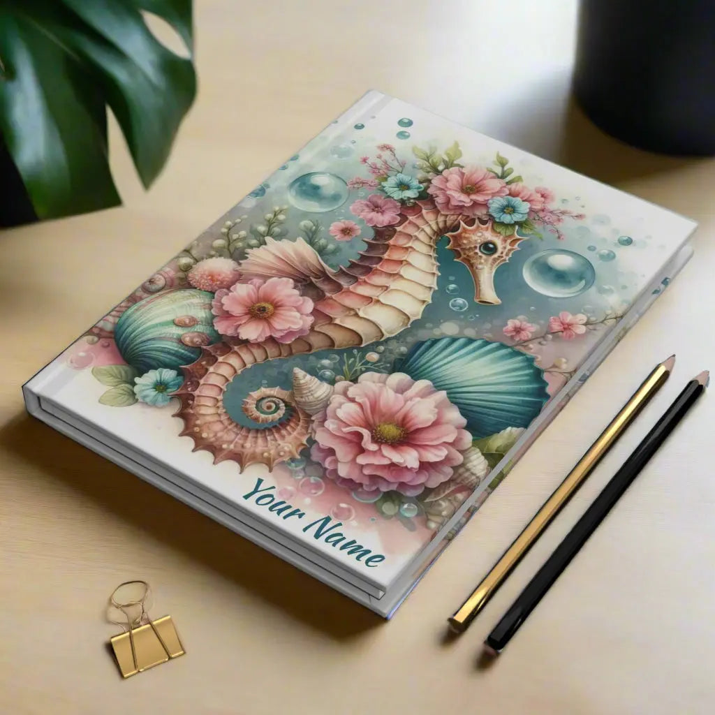 Our hardcover journal brings a touch of ocean magic with a beautifully designed seahorse surrounded by soft, dreamy aqua and pink flowers, bubbles and shells. Perfect for journaling, sketching, or organizing your thoughts, it’s both stylish and durable.