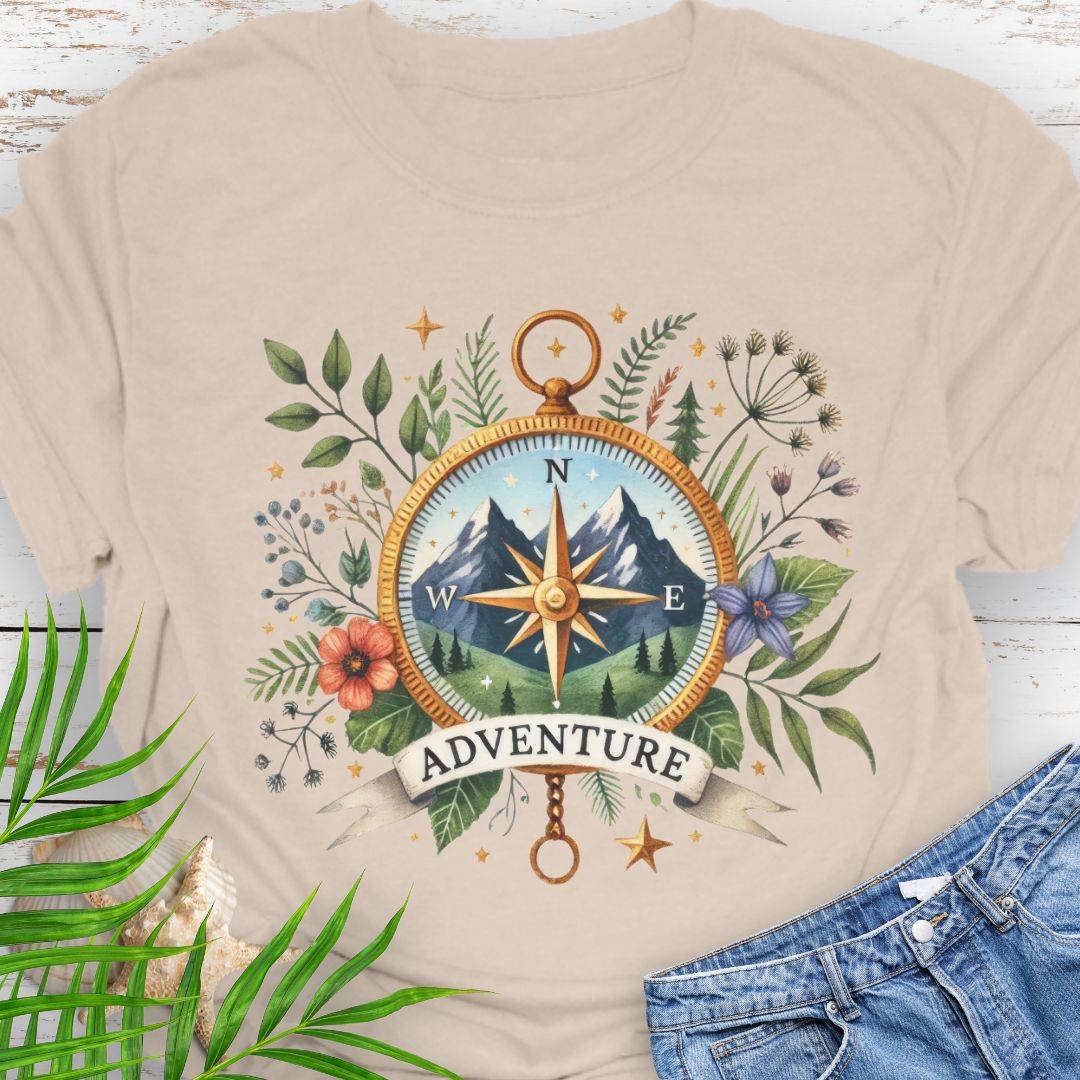 Natural T-shirt with a compass design featuring a mountain scene inside, surrounded by wildflowers and a banner that says "Adventure" – perfect for outdoor enthusiasts.
