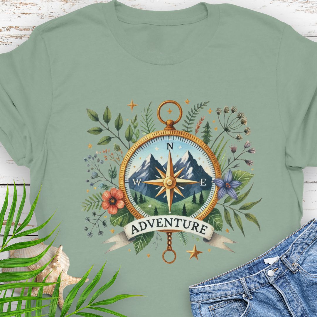 Sage T-shirt with a compass design featuring a mountain scene inside, surrounded by wildflowers and a banner that says "Adventure" – perfect for outdoor enthusiasts.