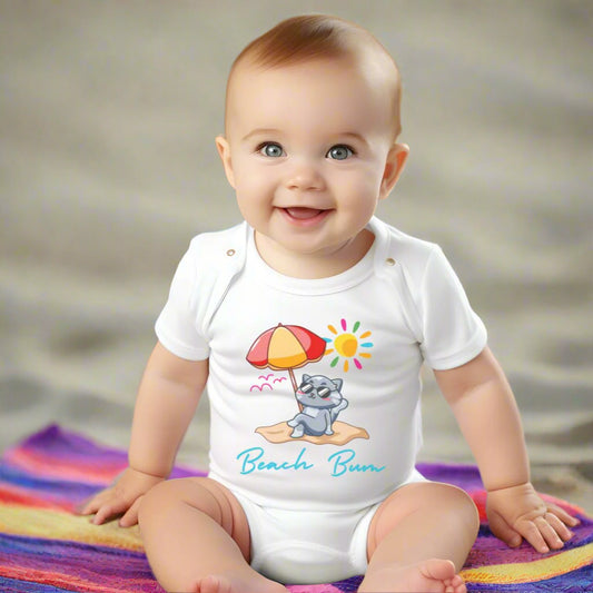 Baby sitting in a white short sleeved bodysuit with a graphic of a cat wearing glasses laying on the beach with an umbrella and the sun. The phrase Beach Bum is written underneath. Perfect for a little beach bum.
