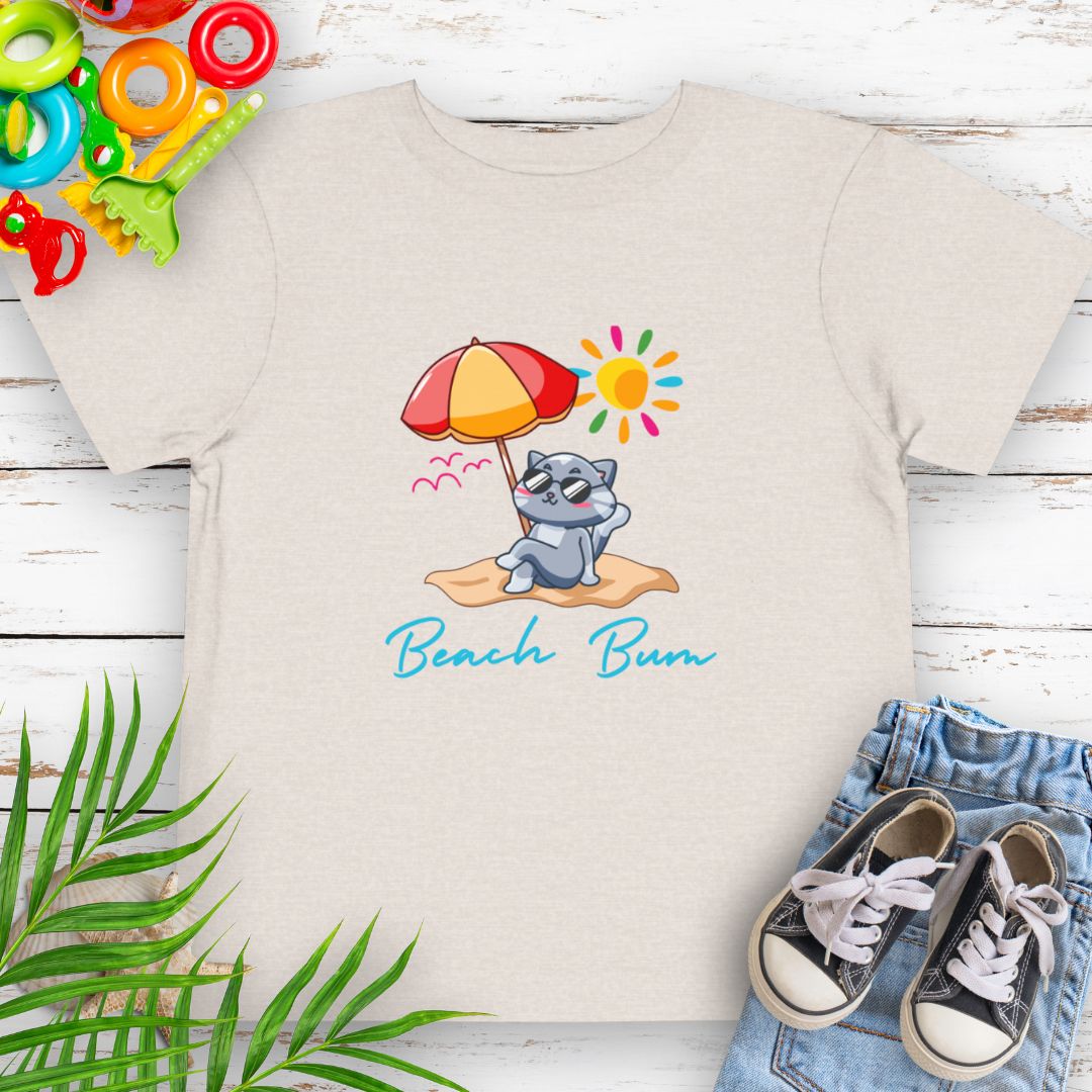 Heather Dust Beach Bum toddler t-shirt with vibrant playful summer design of a cute cat wearing sunglasses laying on the beach under an umbrella.