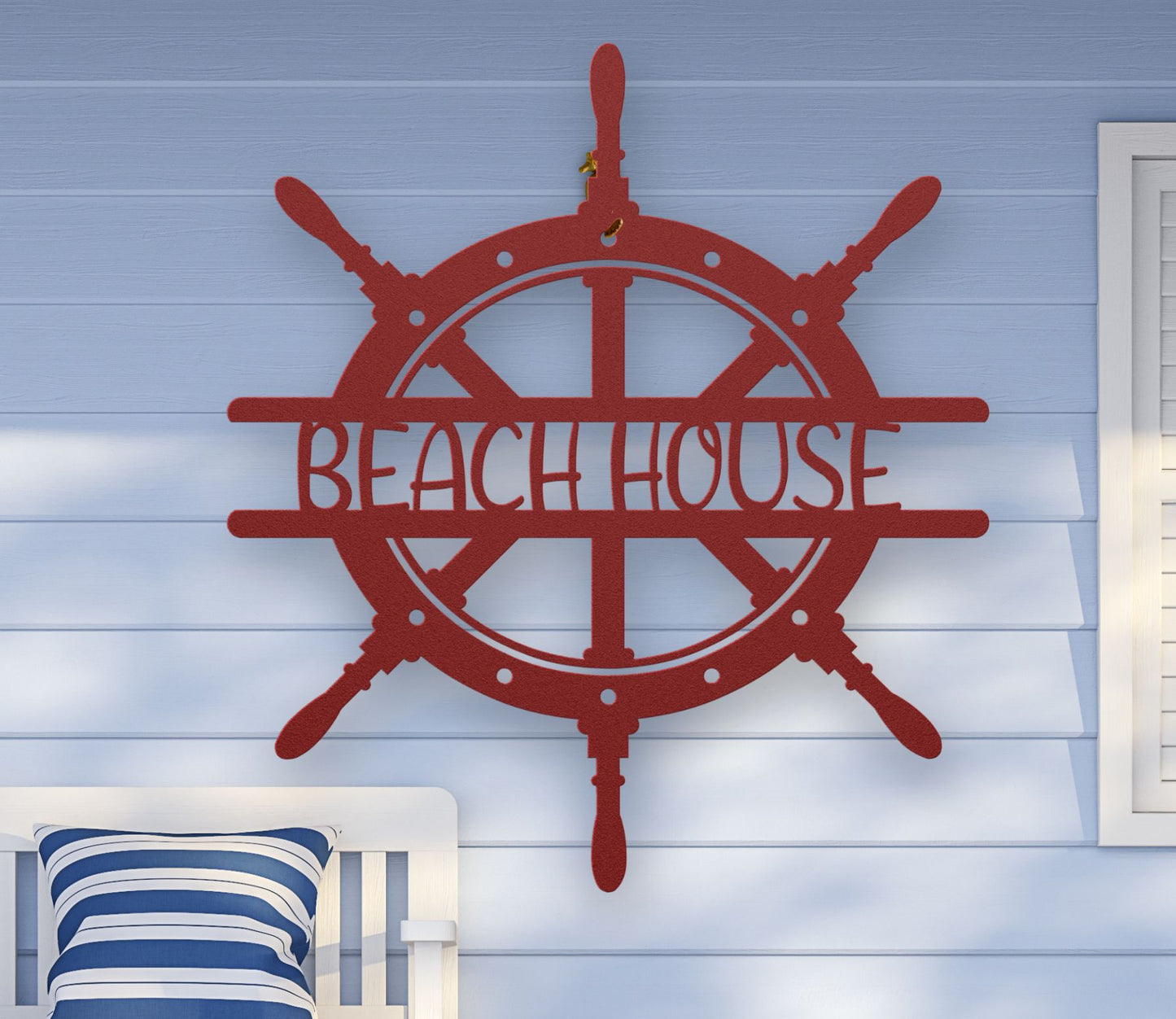 Red metal wall art shaped like a ship wheel with the words “Beach House” cut out in the center, available in multiple colors and sizes.