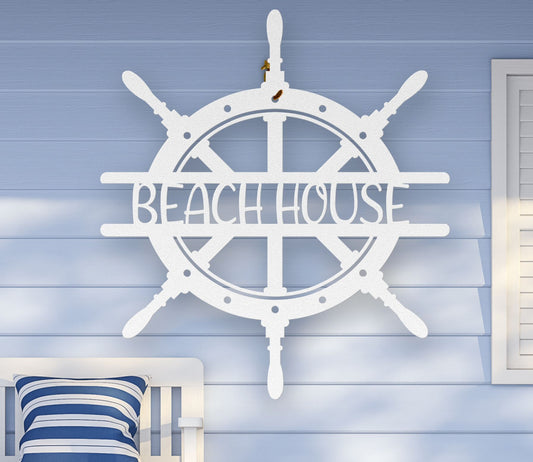 White metal wall art shaped like a ship wheel with the words “Beach House” cut out in the center, available in multiple colors and sizes.