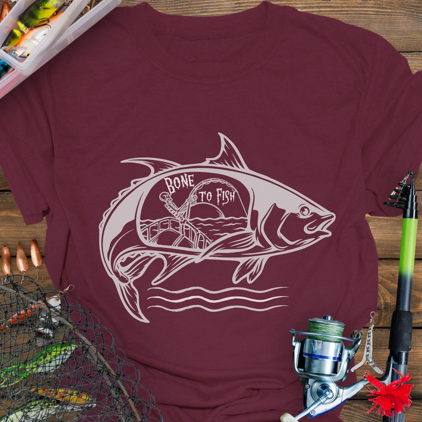 Maroon T-shirt with “Bone for Fishing” text inside a large fish silhouette containing a skeleton fishing off a boat, gothic nautical design for anglers.