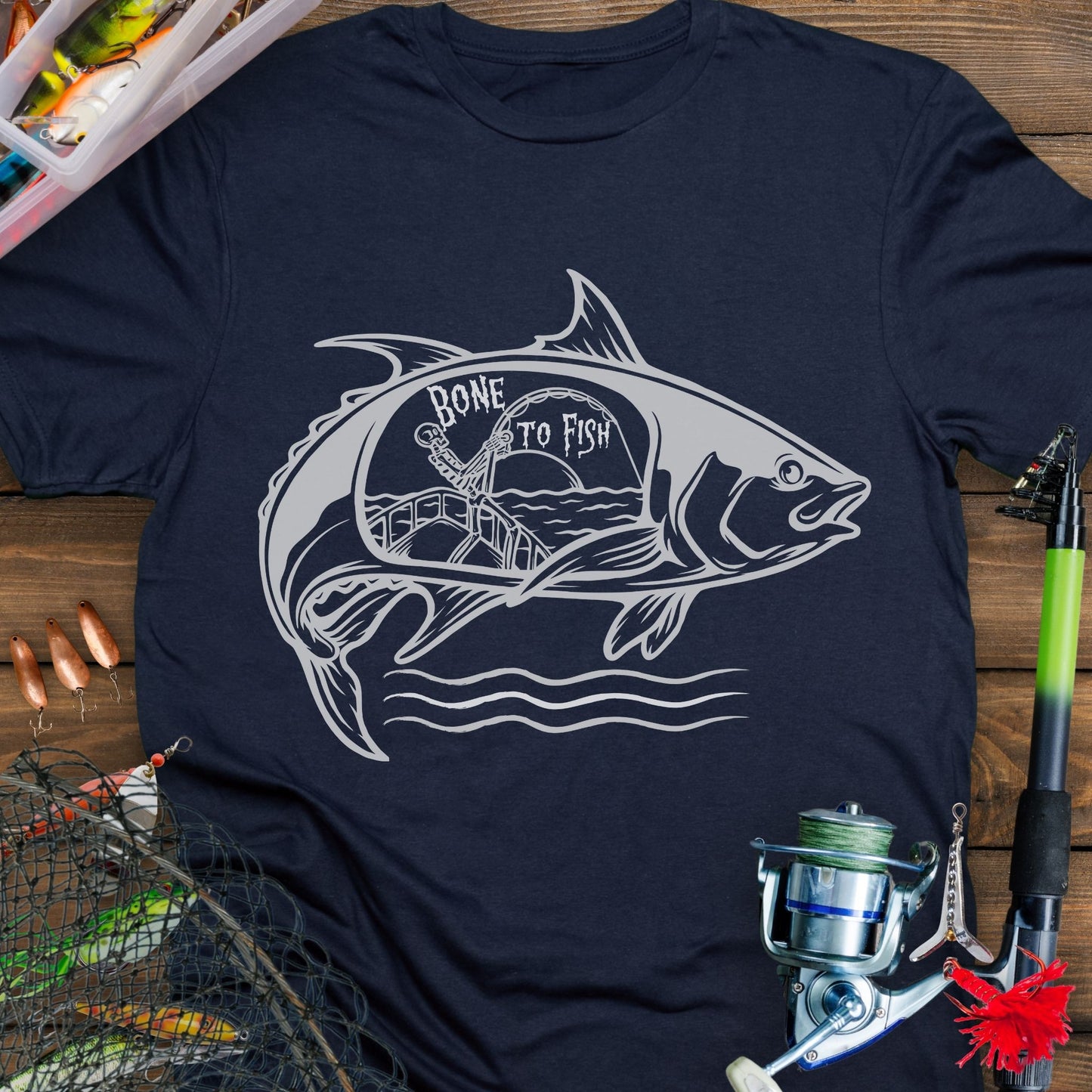 Navy T-shirt with “Bone for Fishing” text inside a large fish silhouette containing a skeleton fishing off a boat, gothic nautical design for anglers.