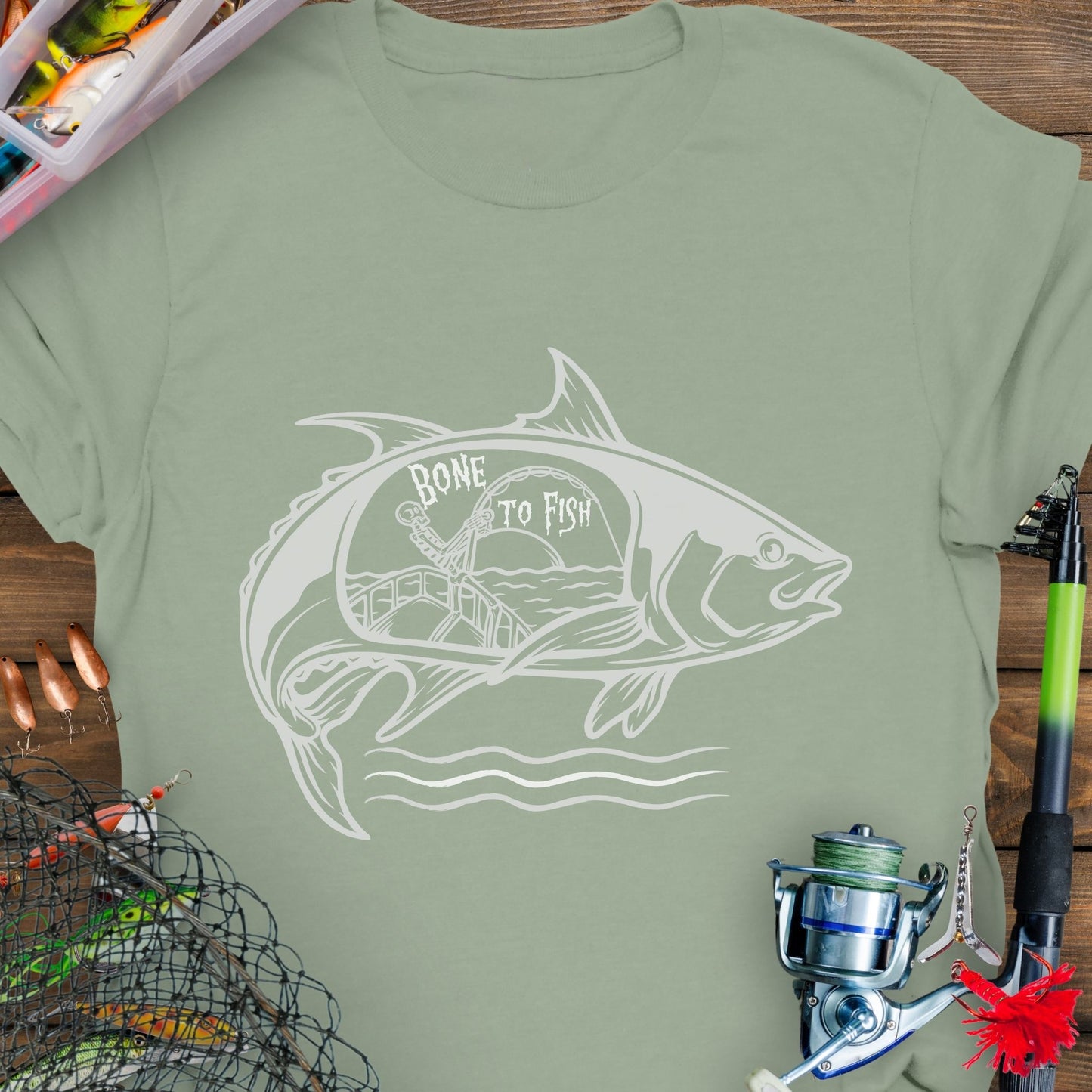 Sage T-shirt with “Bone for Fishing” text inside a large fish silhouette containing a skeleton fishing off a boat, gothic nautical design for anglers.