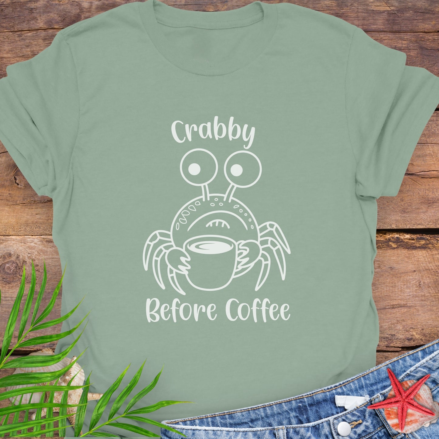 Green t-shirt with a crab graphic and text 'Crabby Before Coffee' on a wooden surface.