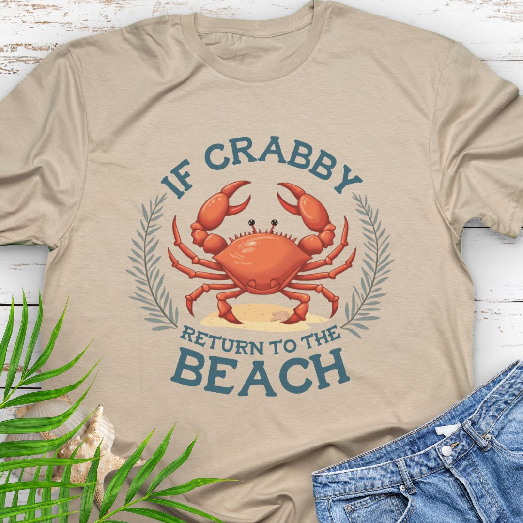 Beige t-shirt with a crab graphic and text 'If Crabby Return to the Beach' on a wooden surface.