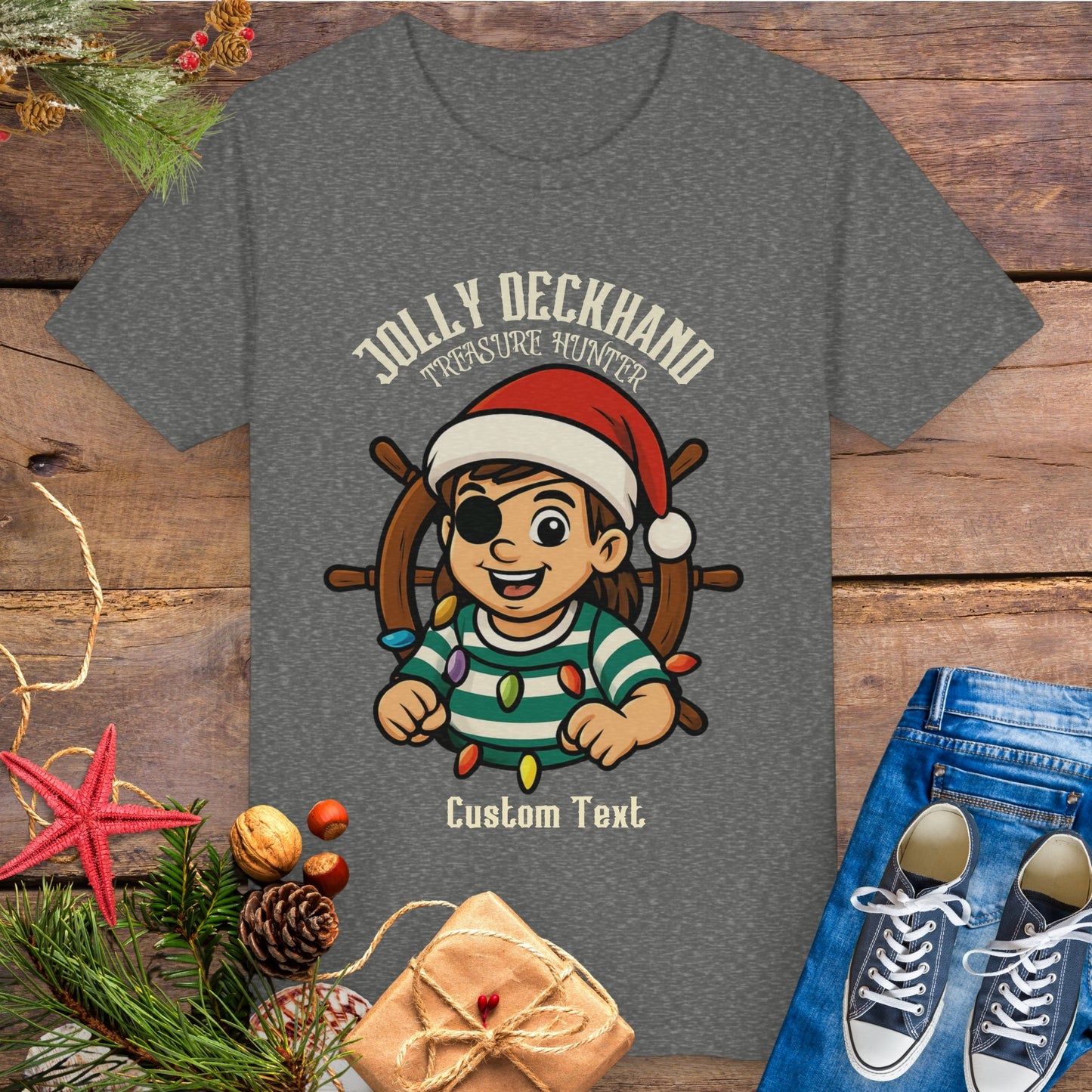 Gray t-shirt with a Christmas-themed design of a girl on a ship's wheel, surrounded by festive items and text 'Jolly Deckhand Treasure Hunter' that can be personalized.