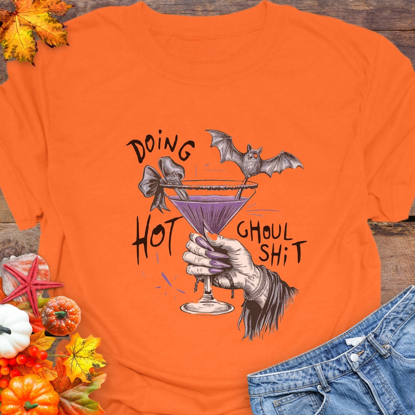 Orange t-shirt with Halloween-themed design featuring a bat, martini glass, and text on a wooden background.
