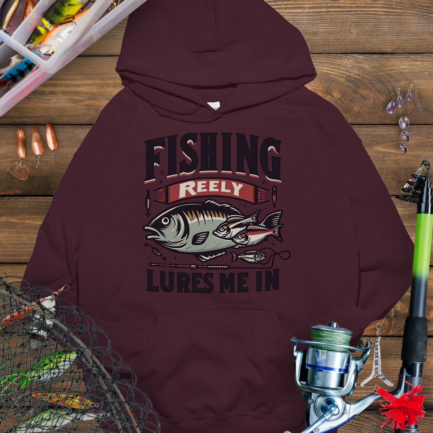 Maroon fishing hoodie with fish and tackle graphics and the phrase “Fishing Reely Lures Me In”.