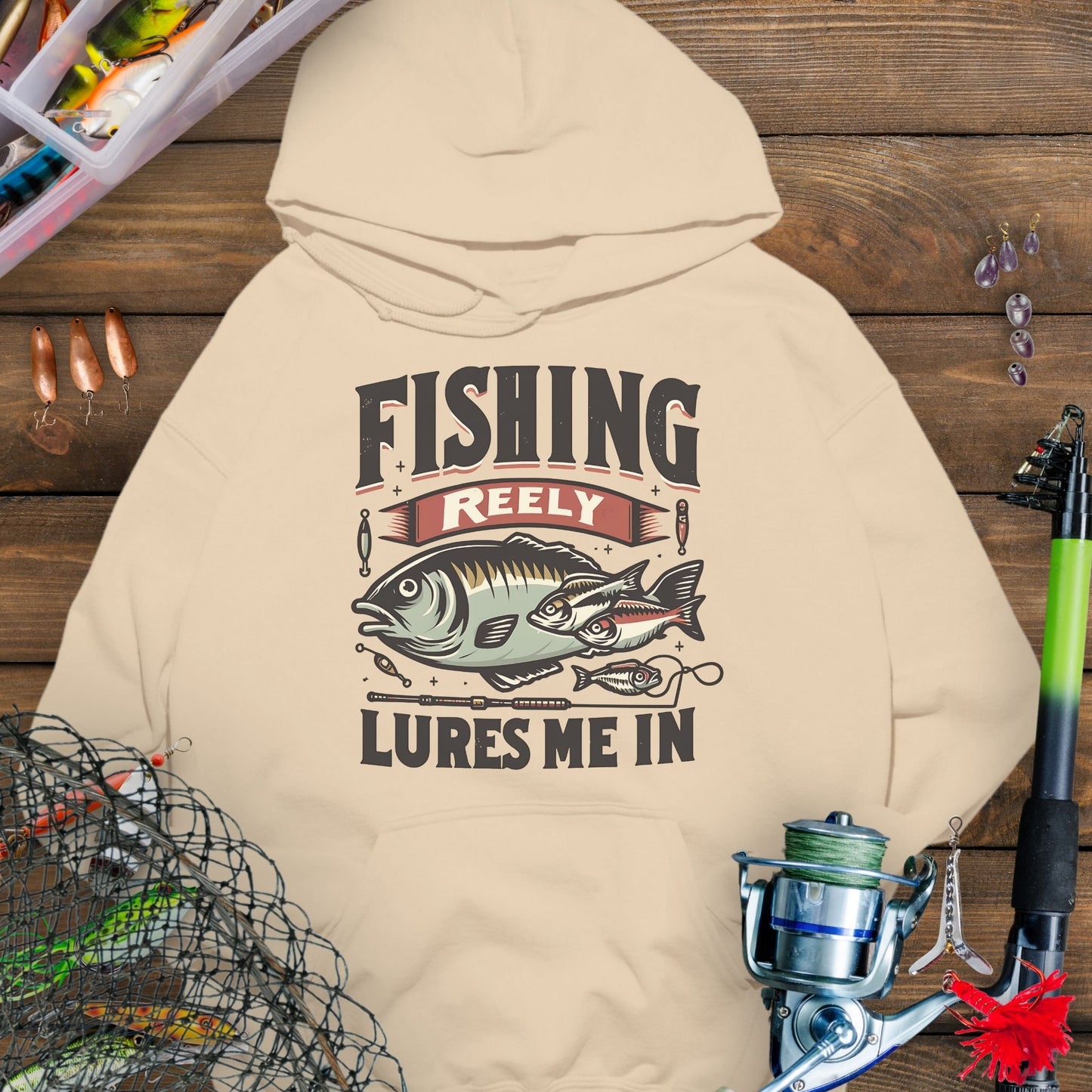Sand fishing hoodie with fish and tackle graphics and the phrase “Fishing Reely Lures Me In”.
