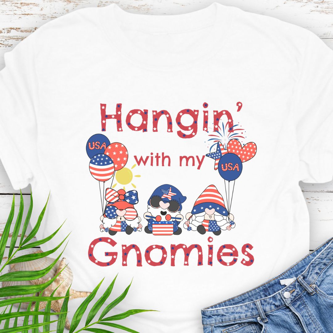 White T-shirt with three gnomes in patriotic outfits holding flag balloons with sun and fireworks in the background with the phrase Hangin' with my Gnomies.