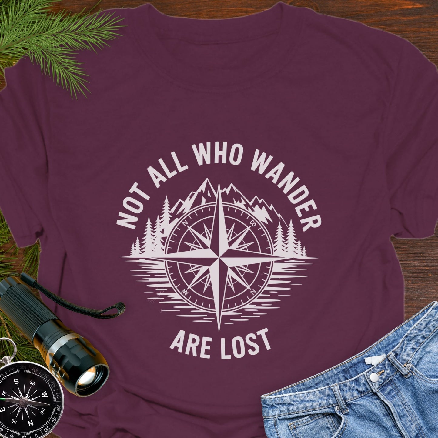 Maroon T-shirt with a mountain range and lake with a compass overlay that says Not All Who Wander are Lost.