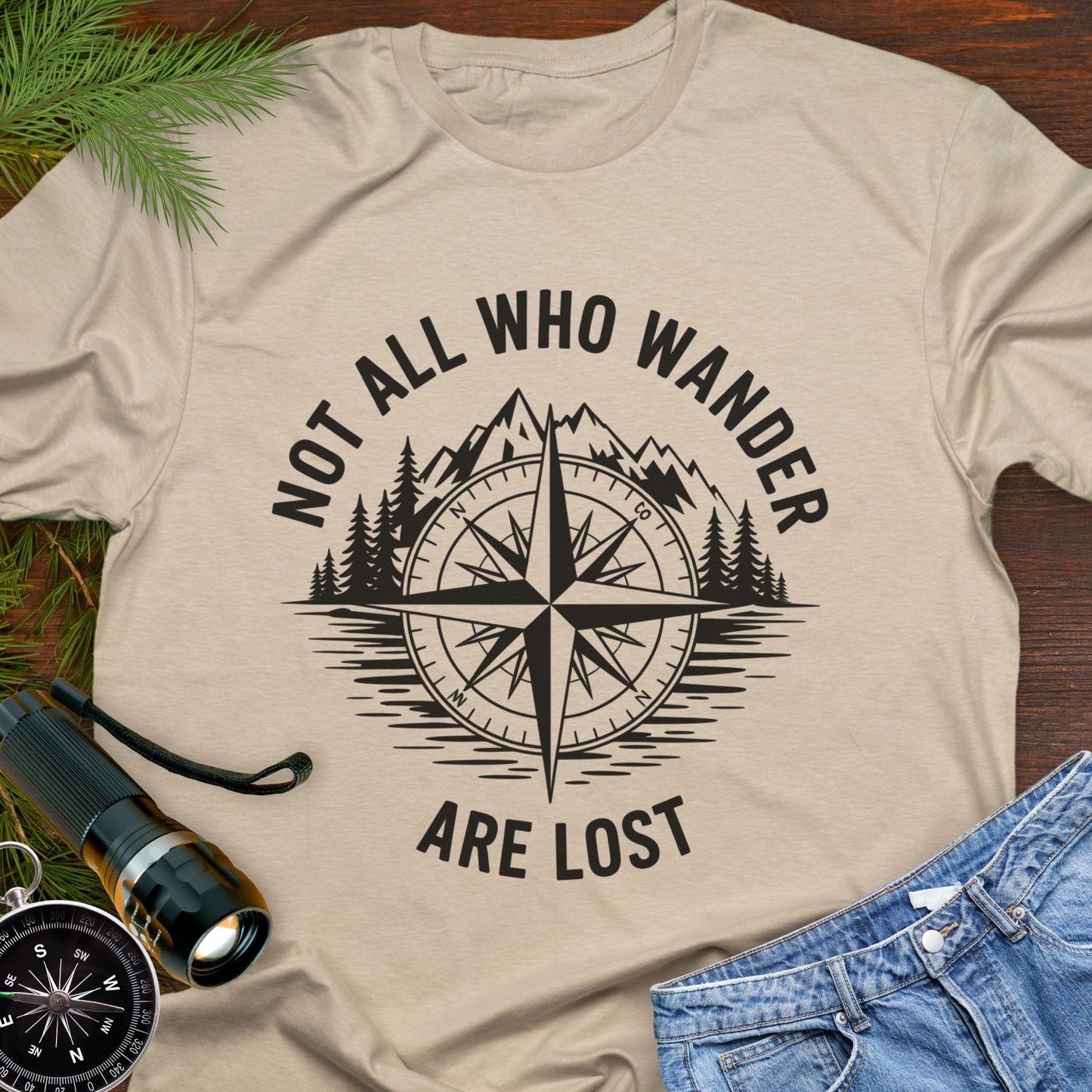 Sand T-shirt with a mountain range and lake with a compass overlay that says Not All Who Wander are Lost.