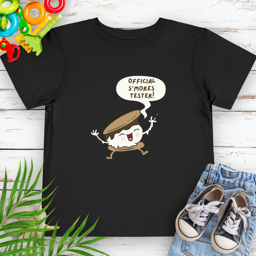 Black Toddler T-shirt with "Official S'mores Tester" text in speech bubble over a S'more character – perfect for camping and summer fun.
