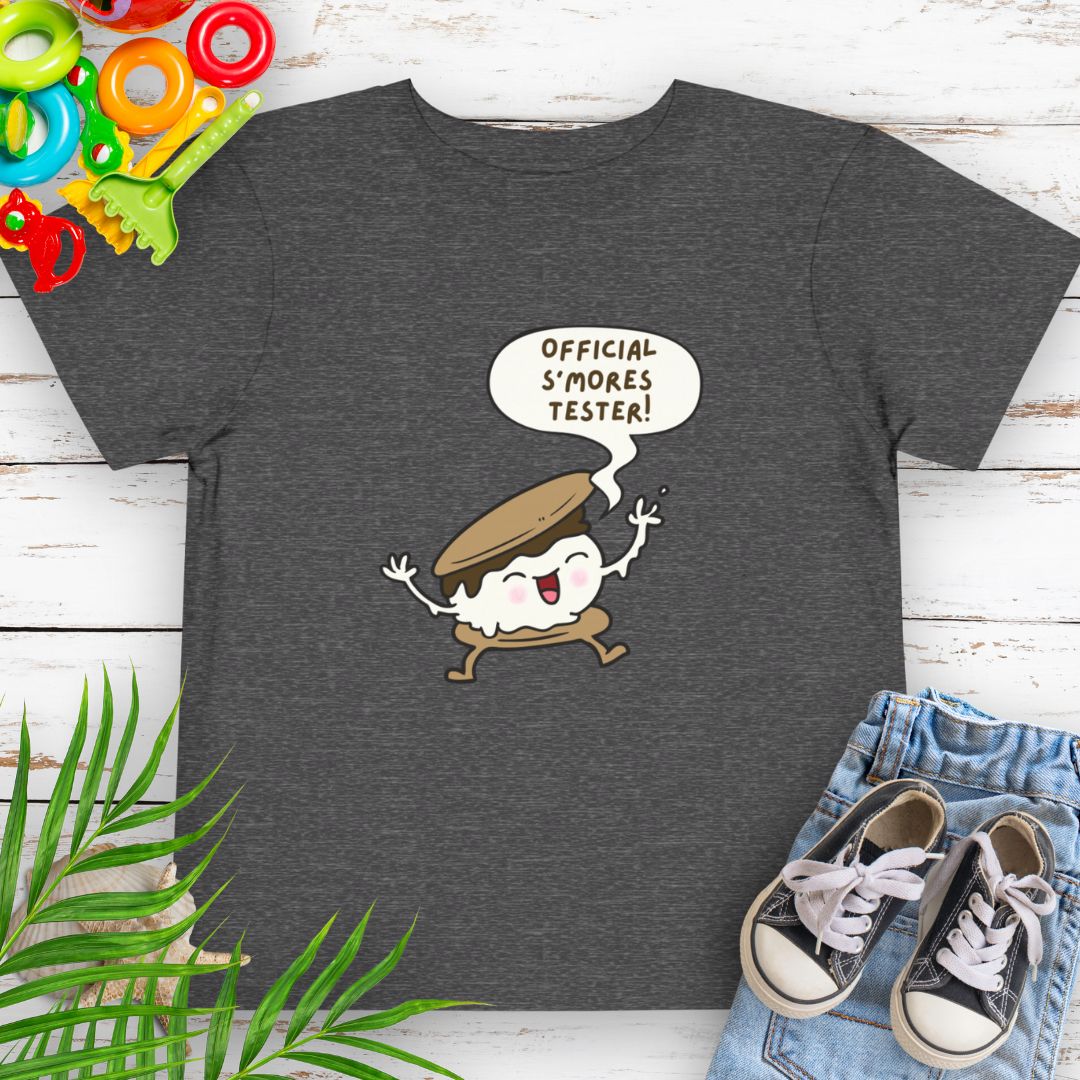 Dark heather grey Toddler T-shirt with "Official S'mores Tester" text in speech bubble over a S'more character – perfect for camping and summer fun.