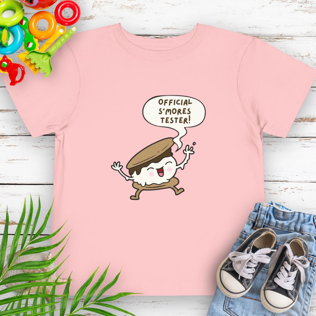 Pink Toddler T-shirt with "Official S'mores Tester" text in speech bubble over a S'more character – perfect for camping and summer fun.