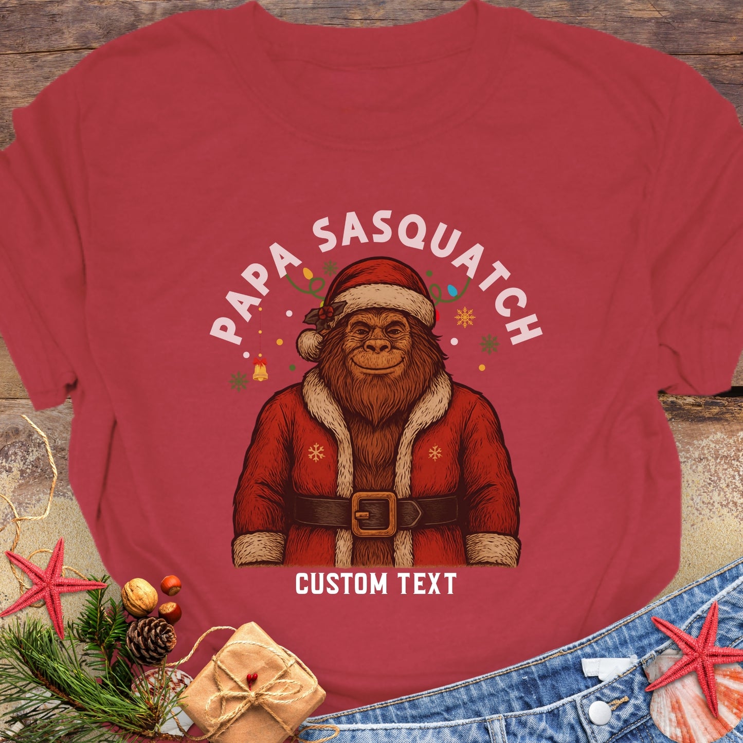 Red t-shirt with a graphic of a Sasquatch in a Santa outfit and 'Papa Sasquatch' text with custom text.