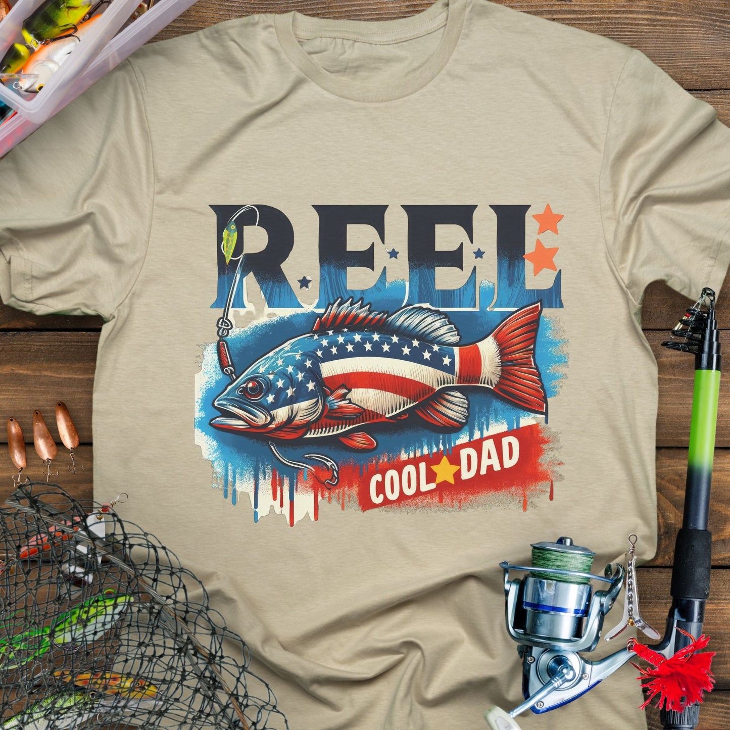 Sand patriotic fishing T-shirt with red, white, and blue design and the phrase “Reel Cool Dad”.