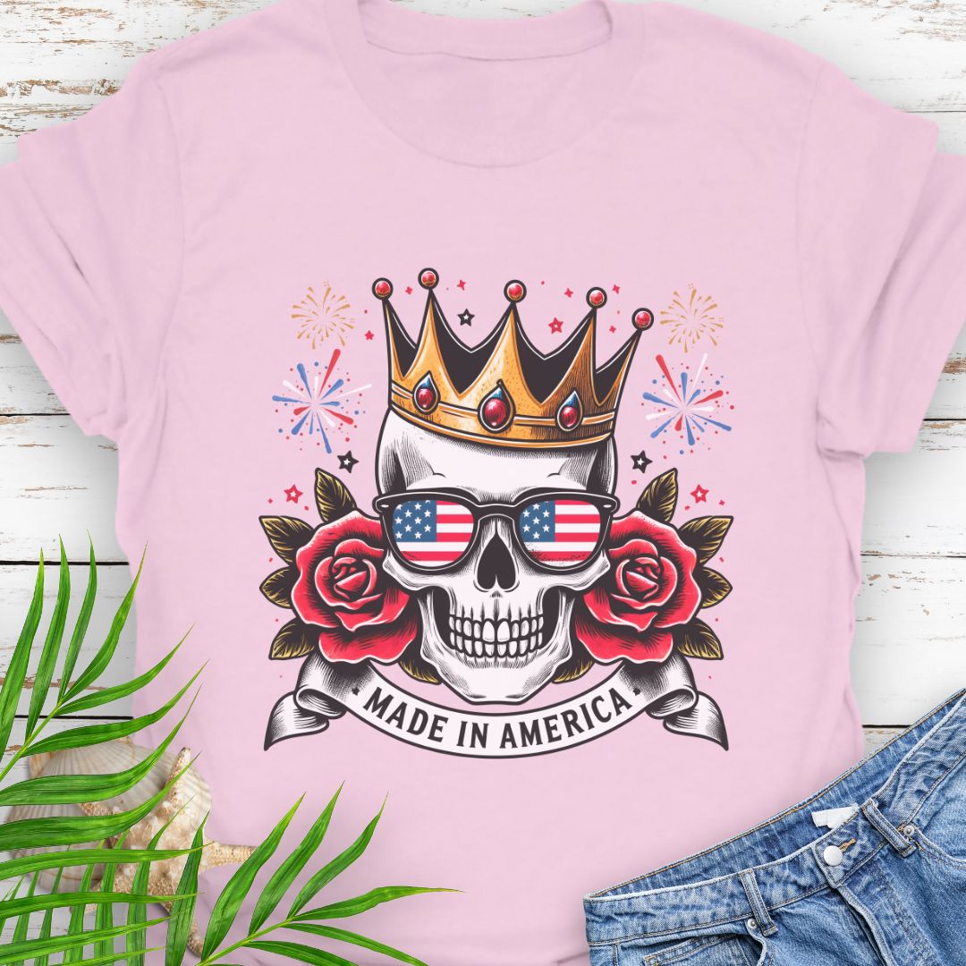 Pink T-shirt with a skull wearing a crown and American flag sunglasses, surrounded by red roses with fireworks in the background and a "Made in America" banner.