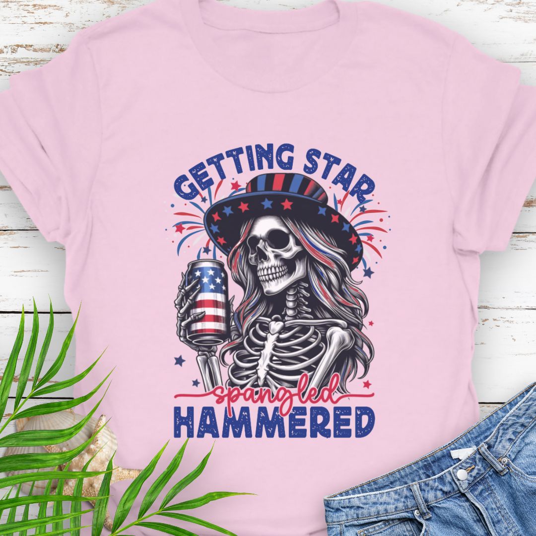 Light Pink T-shirt graphic of a woman skeleton wearing a stars-and-stripes hat, holding an American flag beer can with the phrase “Getting Star Spangled Hammered.