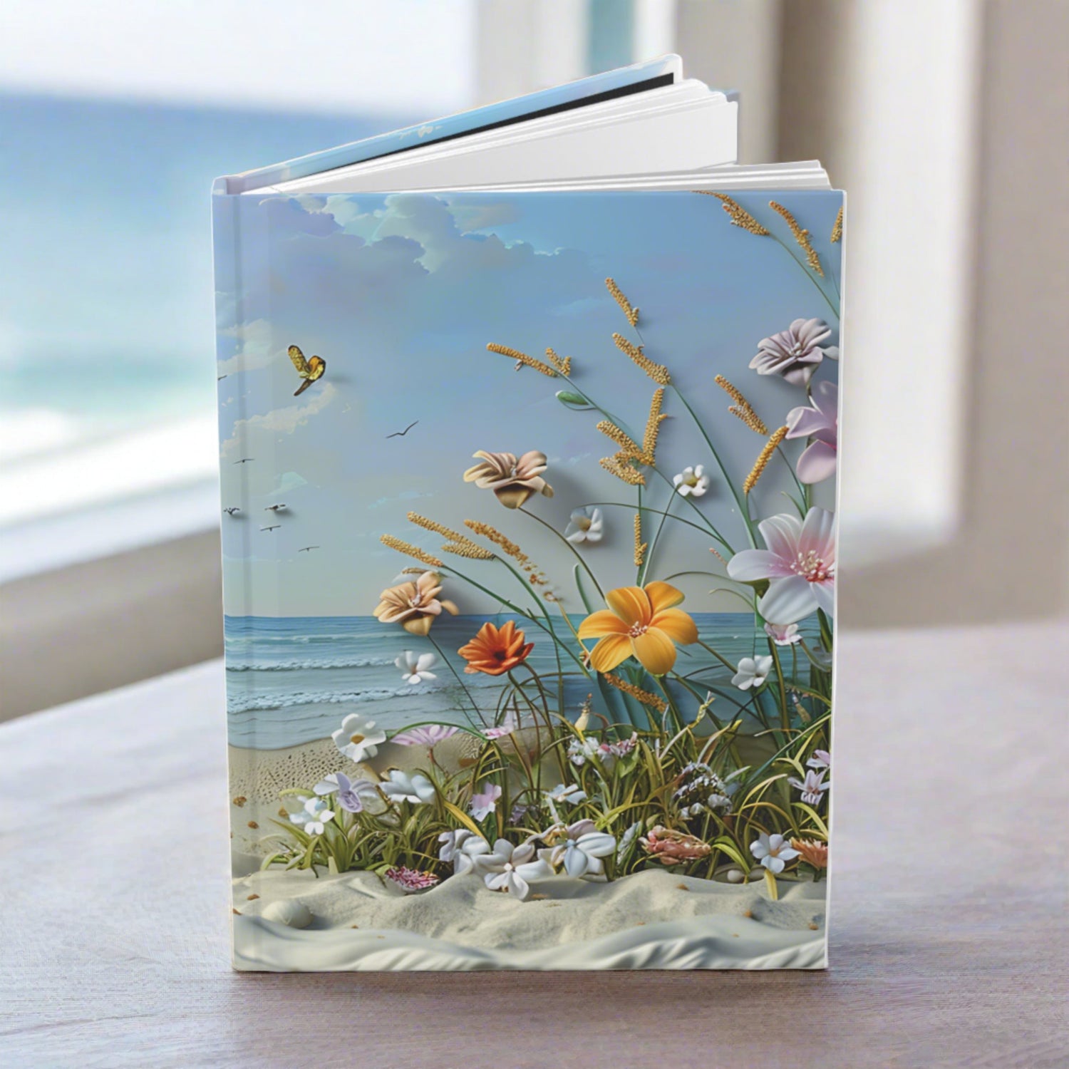 Hardcover journal with a scene of the beach with beach flowers and foliage standing on a table.