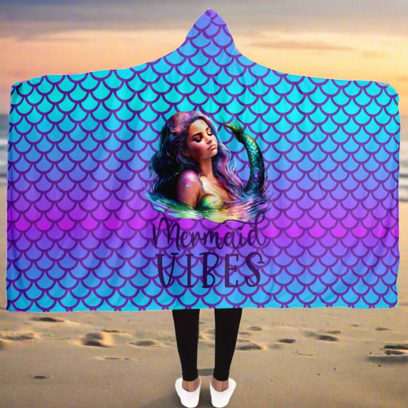 Person wearing a hooded blanket with it stretched open with mermaid scales in purple and turquoise with a picture of a beautiful mermaid with the words mermaid vibes below