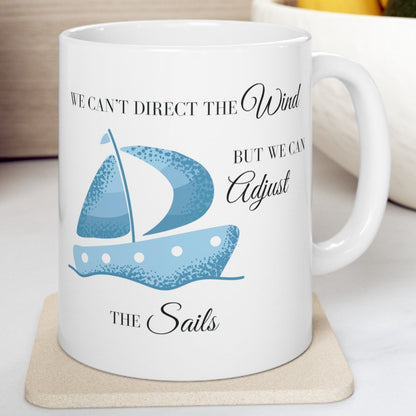 White mug with a blue sail boat that says We Can't Direct the Wind But We Can Adjust the Sails