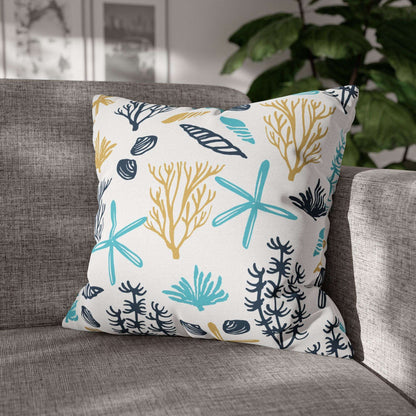 20" x 20" white pillow with coral and starfish pattern on a gray couch.