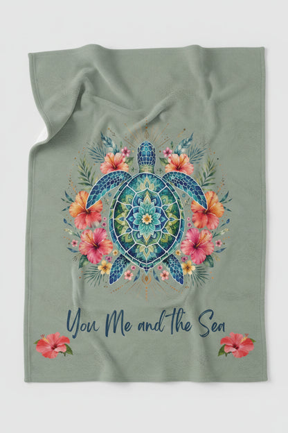 An ultra-soft plush throw blanket featuring a vibrant mandala sea turtle surrounded by tropical hibiscus flowers with the phrase "You, Me and the Sea" on a sage-green background.