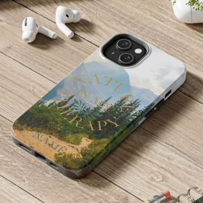 Phone case with 'Nature Therapy' design on a wooden desk with laptop, earbuds, and notebook.