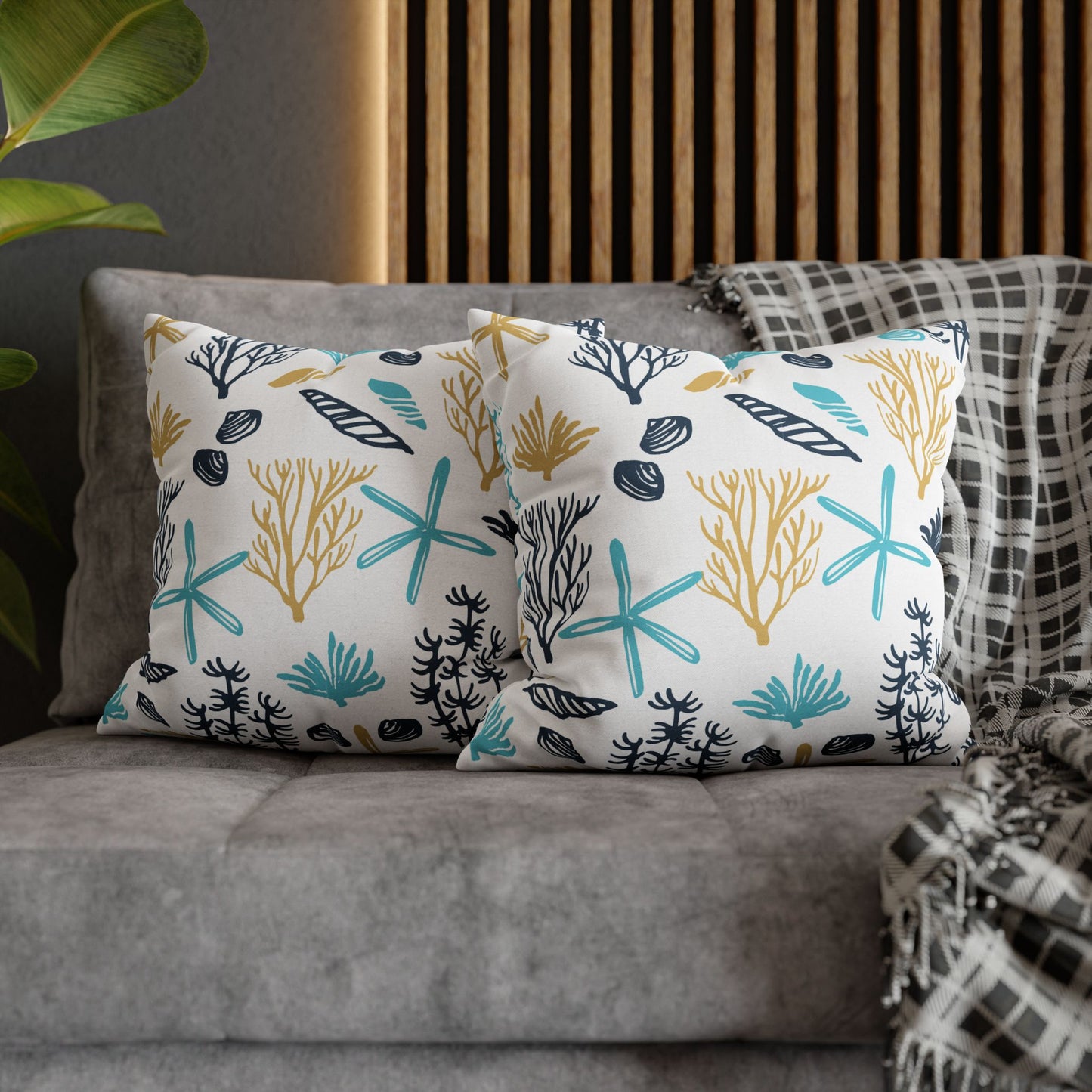 Two 18" x 18" white pillows with coral and starfish pattern on a gray couch.