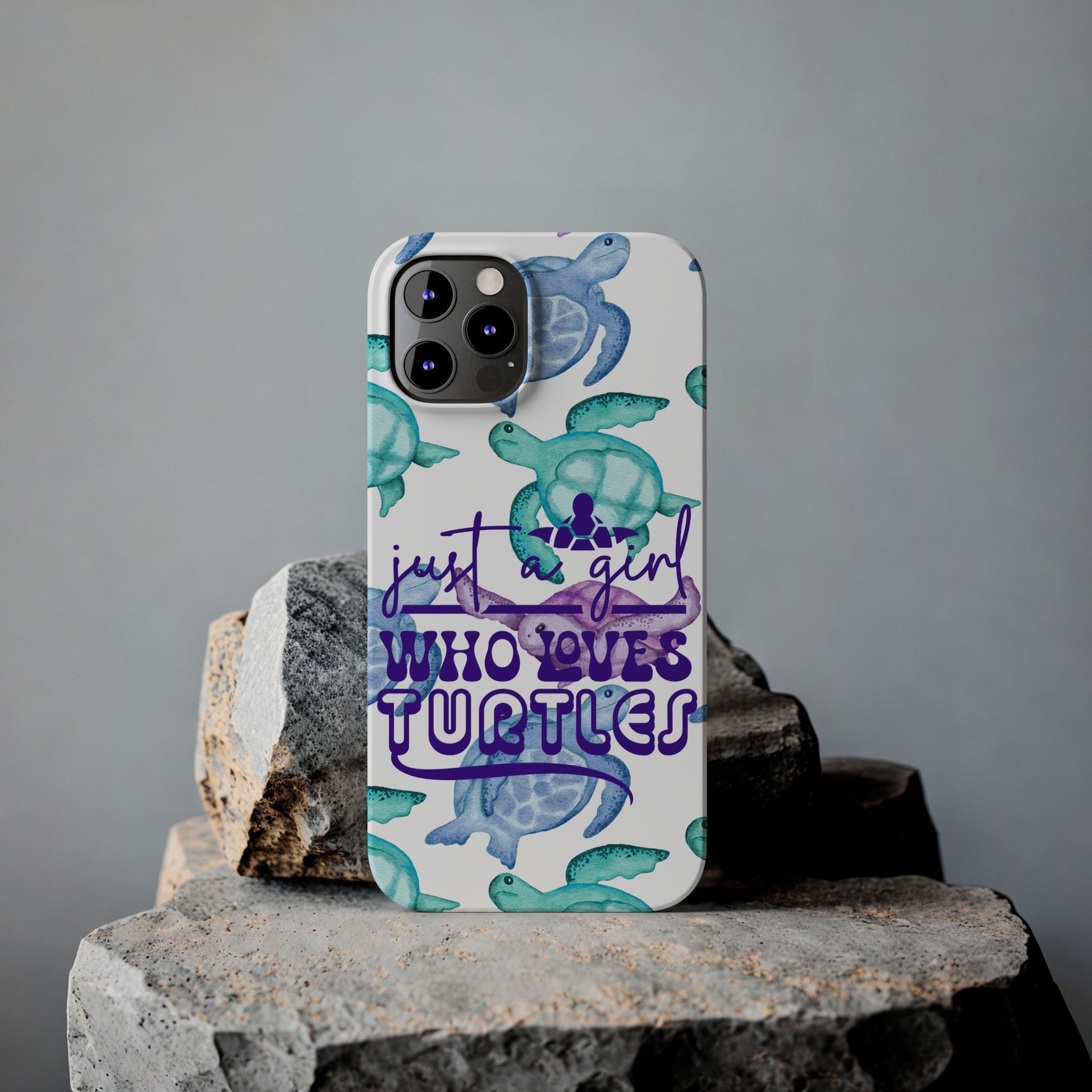 Iphone case with turquoise, blue and purple sea turtles that says  Just a Girl Who Loves Sea turtles laying against rock