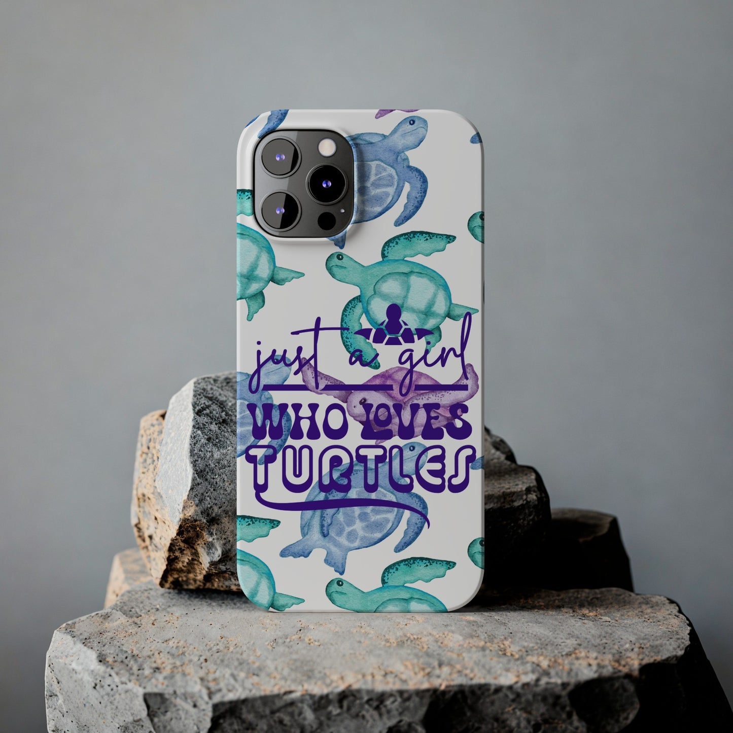 Iphone case with turquoise, blue and purple sea turtles that says  Just a Girl Who Loves Sea turtles laying against rock