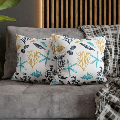 Two 16" x 16" white pillows with coral and starfish pattern on a gray couch.