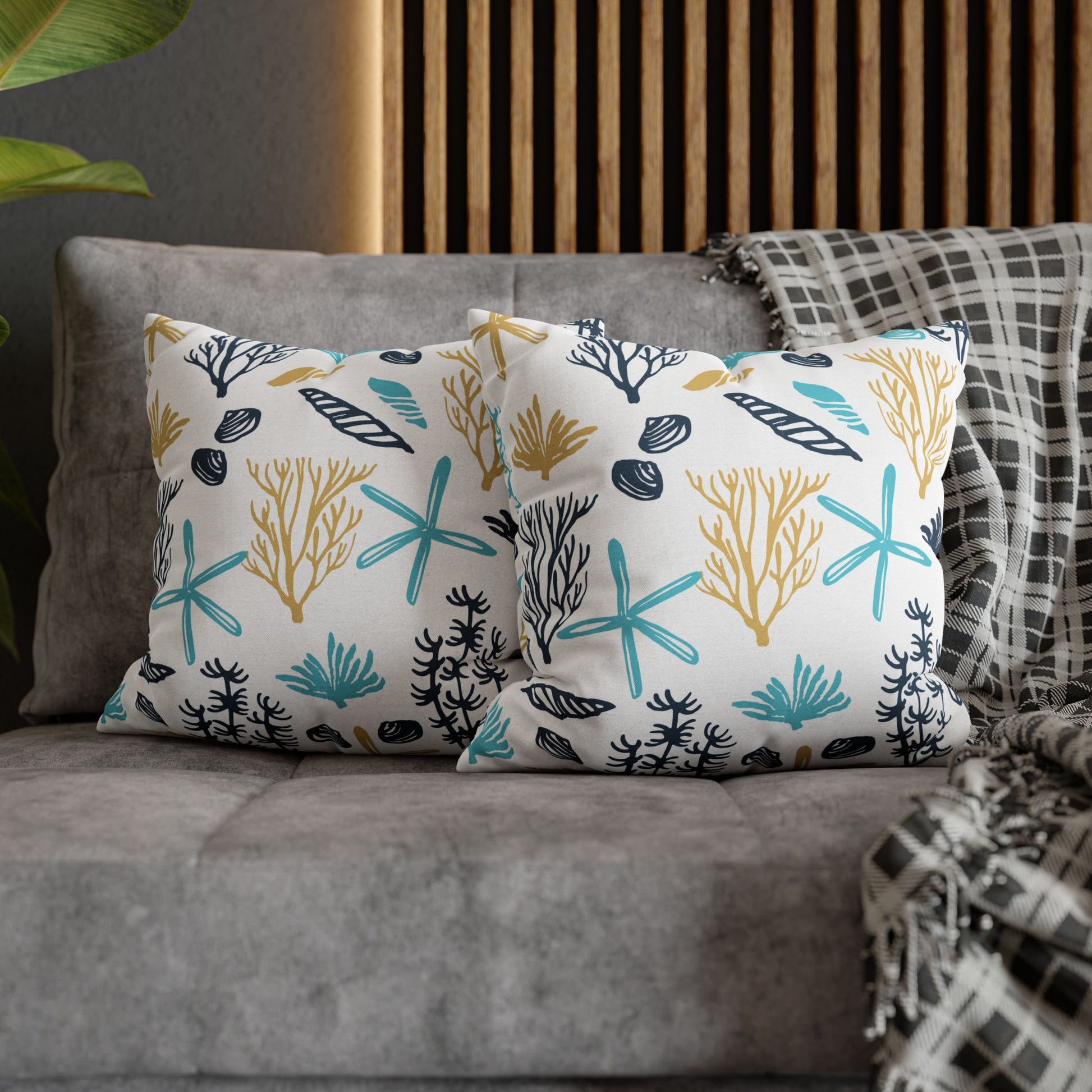 Two 16" x 16" white pillows with coral and starfish pattern on a gray couch.