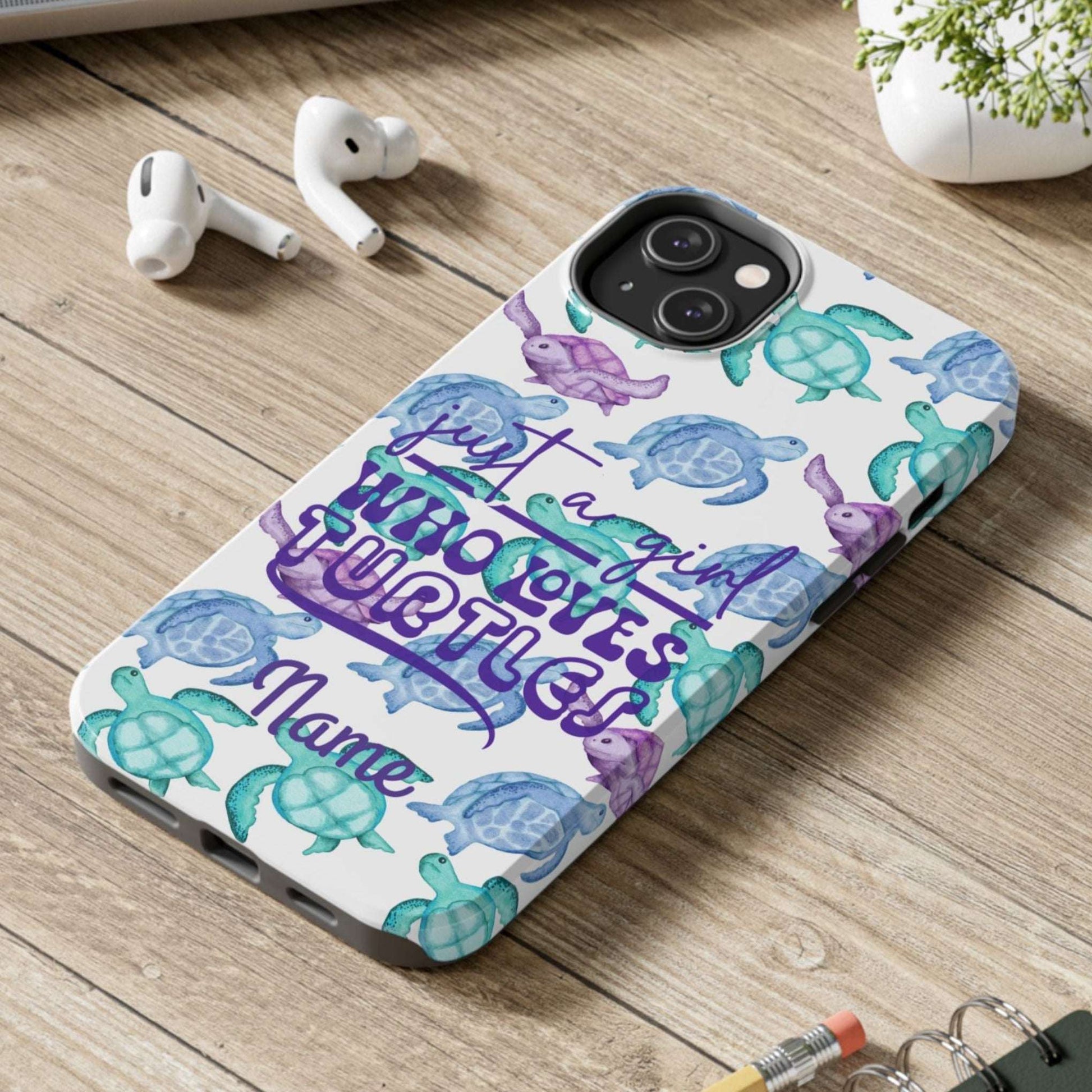 Phone case with sea turtle design on a wooden surface with laptop, earbuds, and notebook.