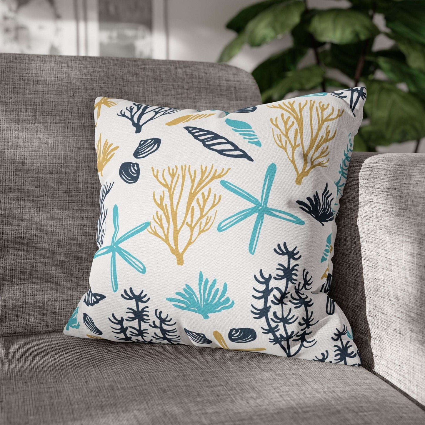 Decorative 18" x 18" white pillow with coral and starfish pattern on a gray couch.