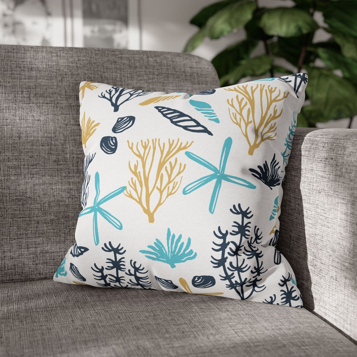 Decorative 18" x 18" white pillow with coral and starfish pattern on a gray couch.