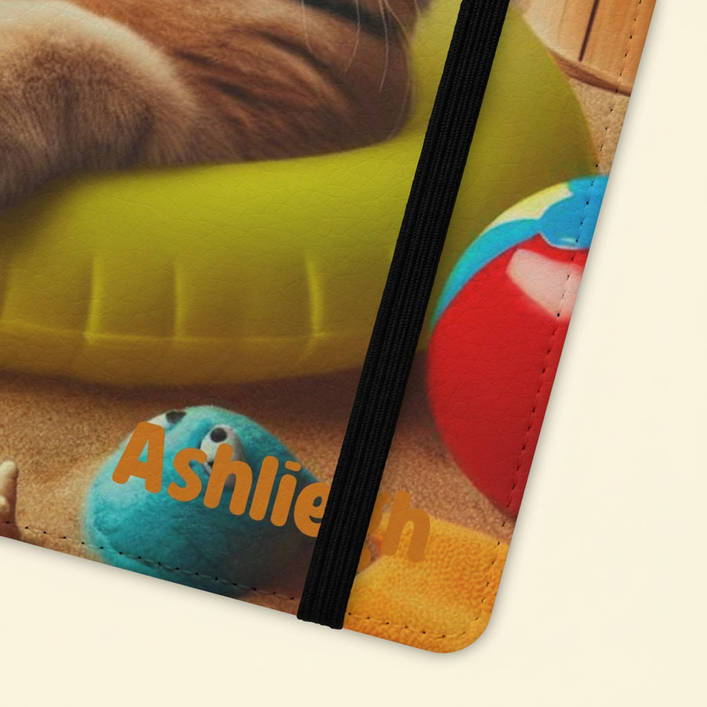 Close-up of corner showing stitching and elastic band on flip phone case with an illustration of a cat lying in an inner tube on the beach with the text “Pawsitive Vibes,” customizable with a name.