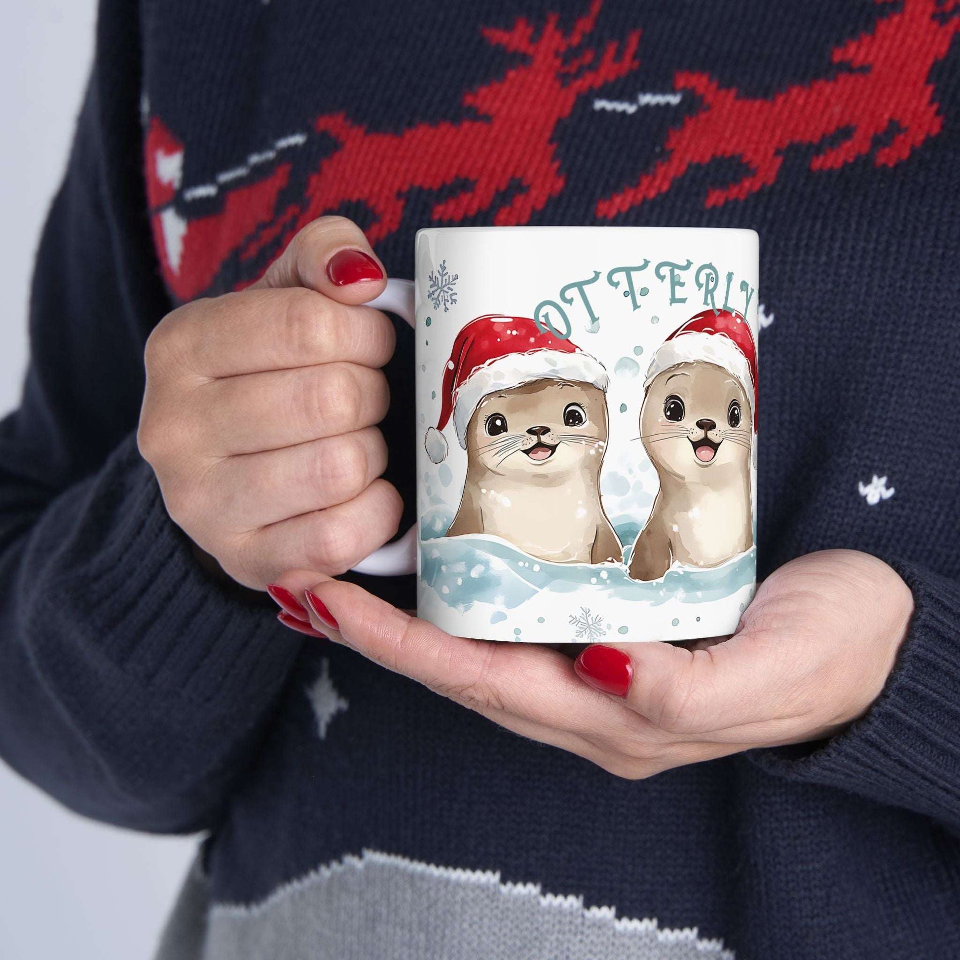Person holding a mug with otters wearing Santa hats against a festive sweater background