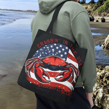 A black tote bag with an American Flag design with a crab coming out and says Crabbin' in the USA and Crescent City, CA.  